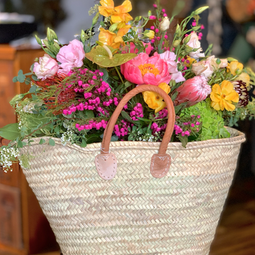 An arrangement of fresh blooms in a wicker basket with leather handles.